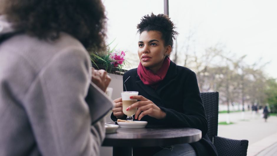 Duas amigas conversando num café ao ar livre, num dia claro